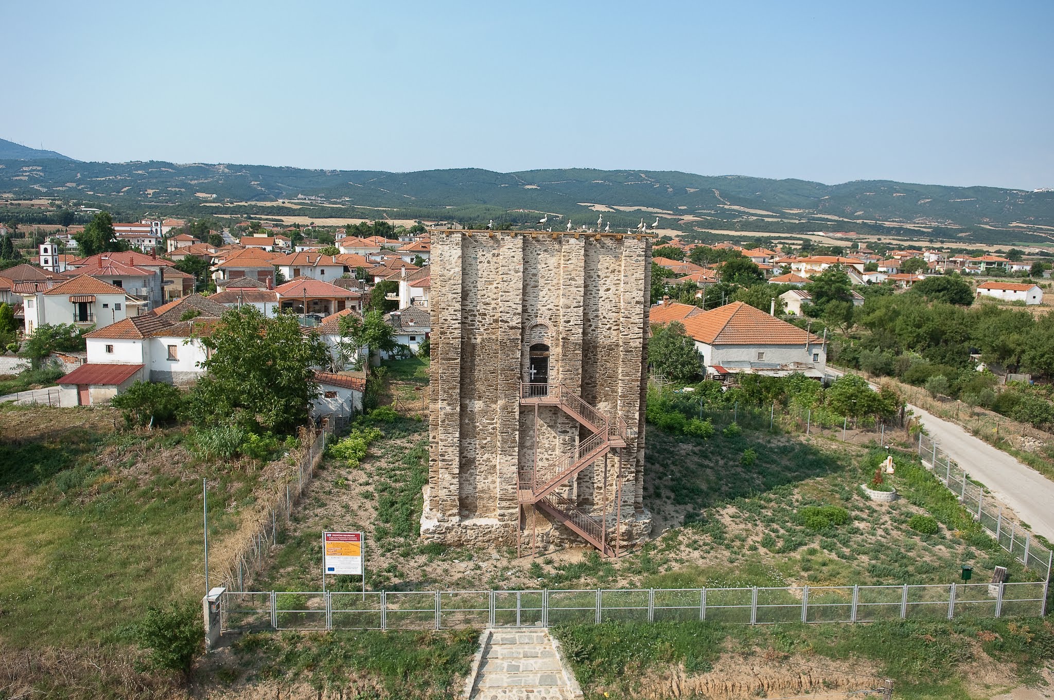 An aerial view of the Byzantine Tower of Marianos, situated at the edge of a village with several storks nesting on its rooftop.