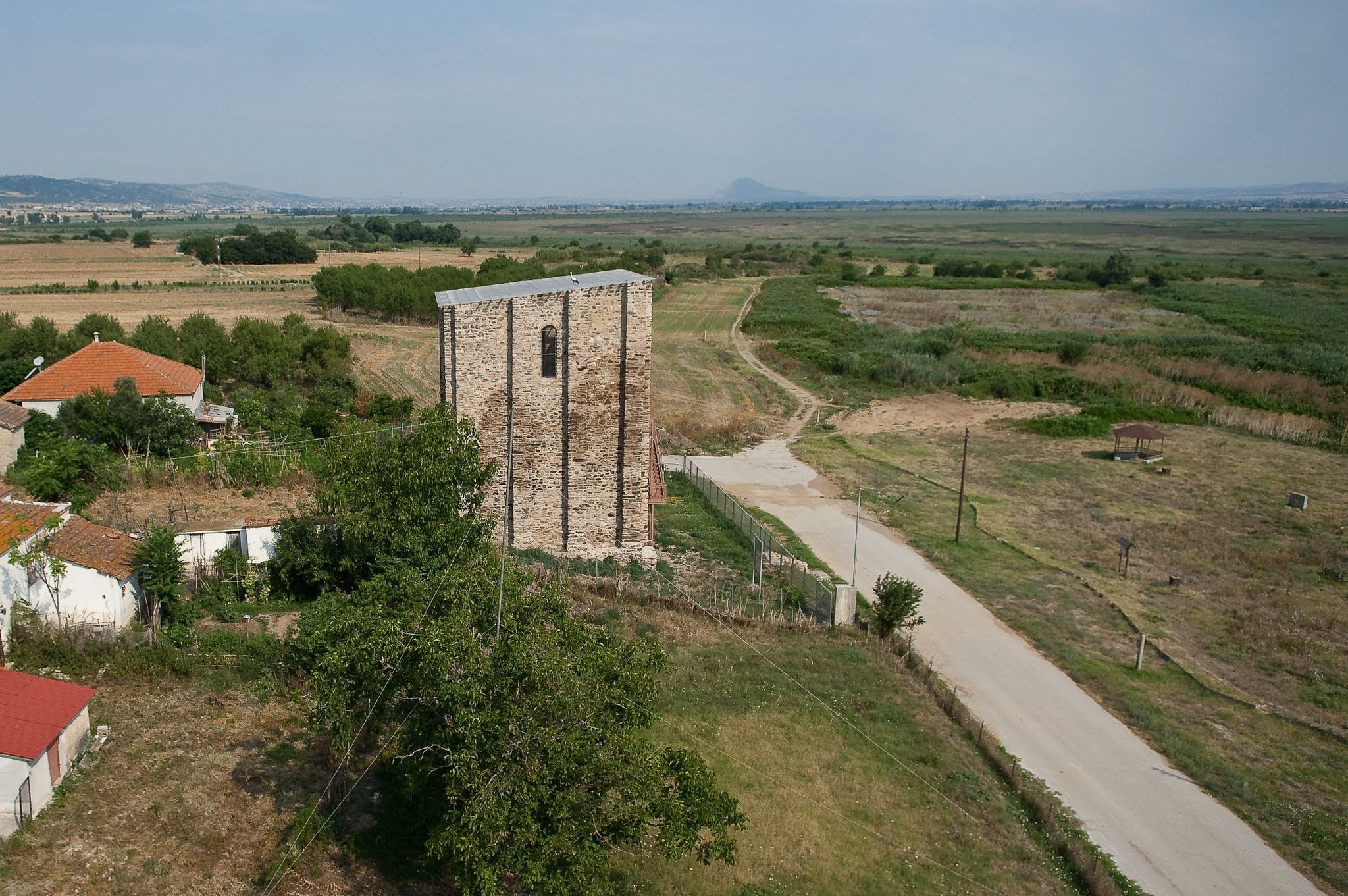 An aerial view showing the side facade of the Tower of Marianos, looking out over the surrounding agricultural plains and wetlands.