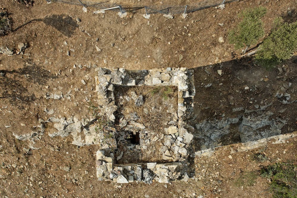 A top-down aerial photograph of the rectangular stone foundation ruins of an ancient building or tower situated in a dry, rocky field.