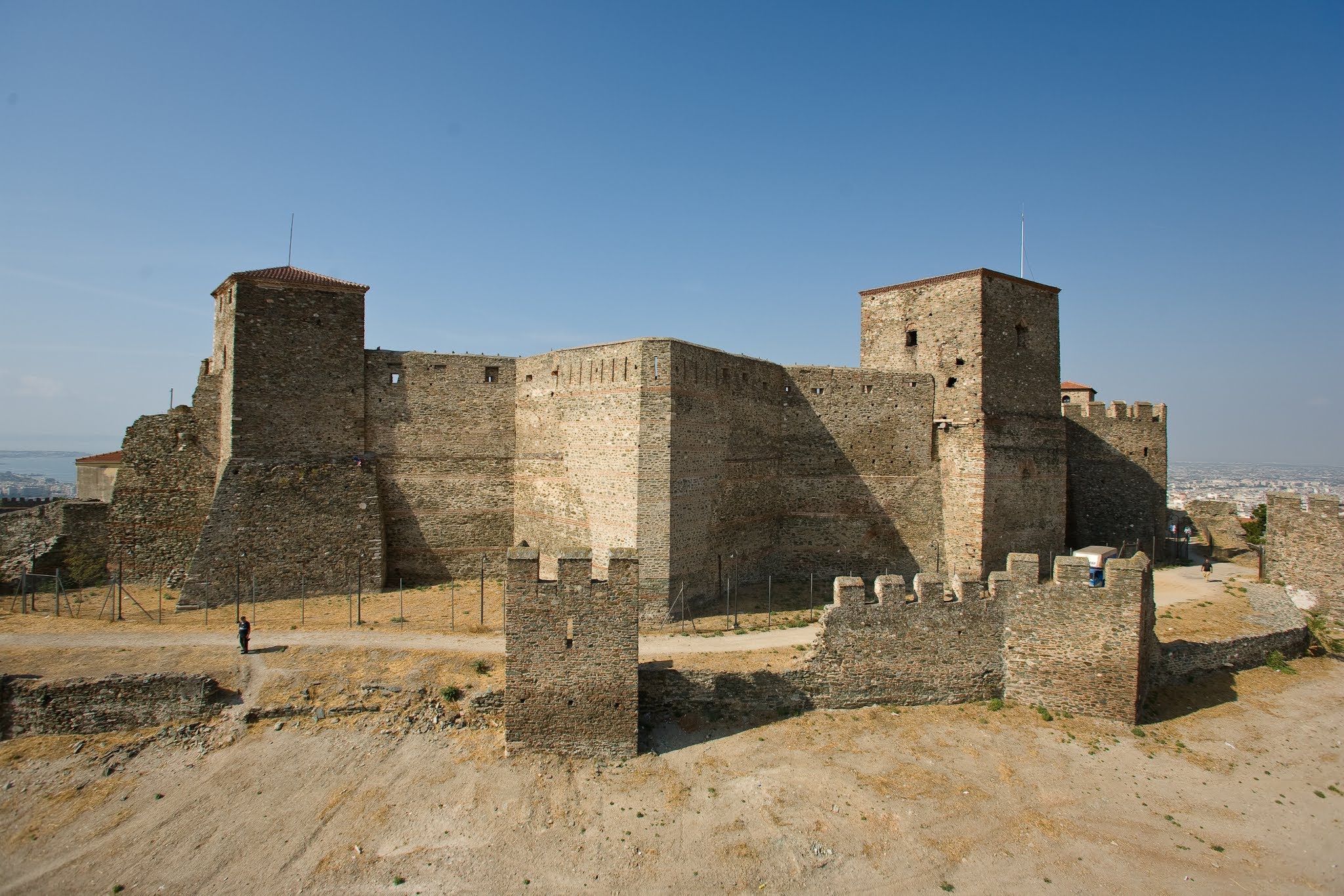 An elevated view of the historic Heptapyrgion fortress in Thessaloniki, showing its massive stone walls, towers, and ramparts under a clear blue sky.