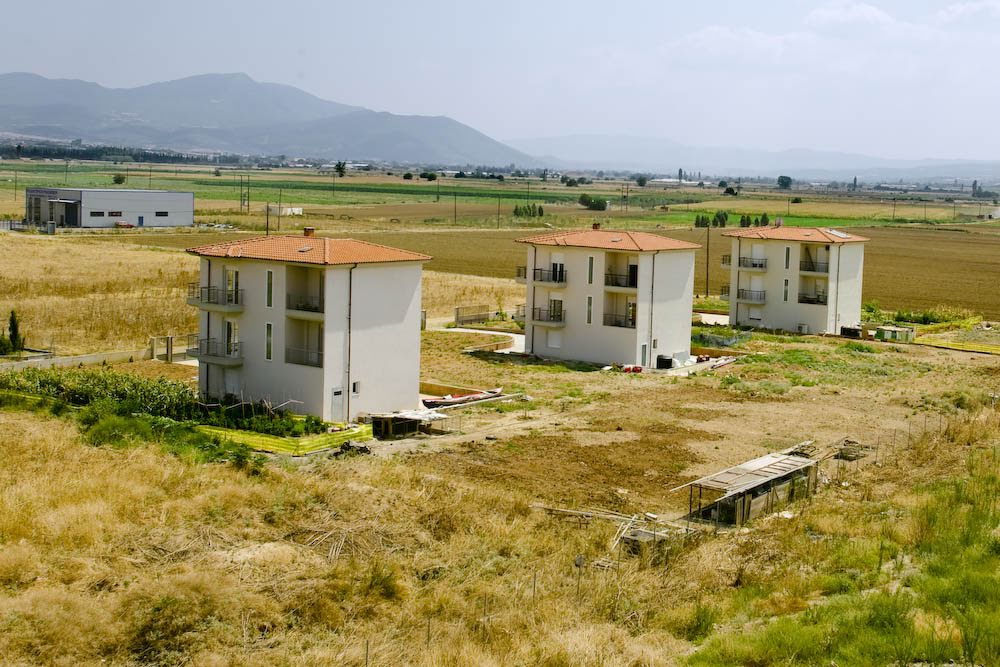 Aerial view of three modern multi-story residential buildings set in a rural countryside landscape with distant mountains.