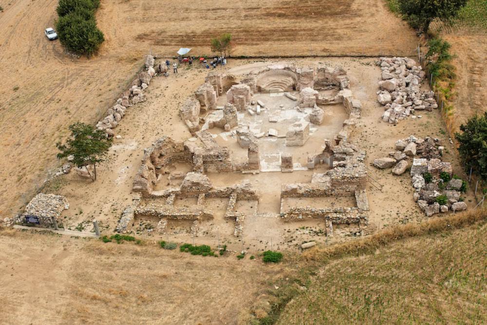 An aerial view of an archaeological excavation site featuring the stone foundations and ruins of an ancient circular or octagonal building.