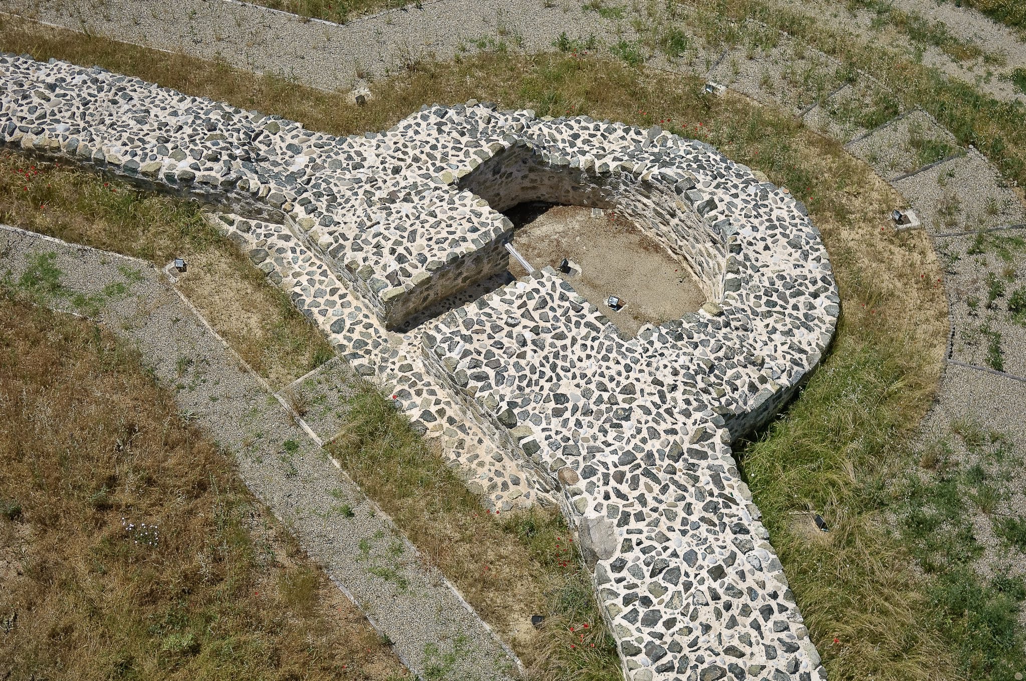 Aerial perspective of stone ruins and archaeological foundations showcasing a circular masonry design surrounded by landscaped gravel paths.