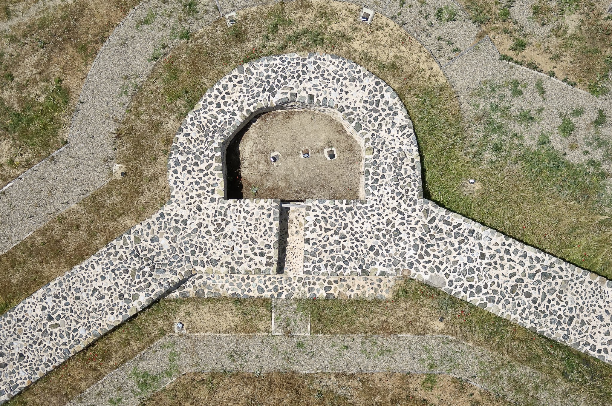 Symmetrical top-down aerial photograph of a semi-circular stone masonry foundation and surrounding gravel pathways.