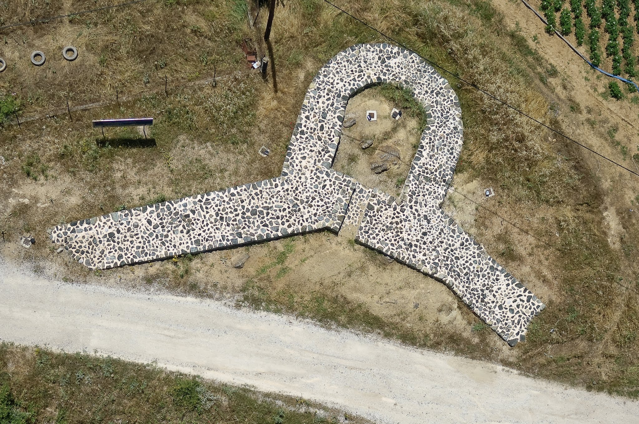 Top-down aerial photograph of a keyhole-shaped stone pavement feature next to a rural dirt road.