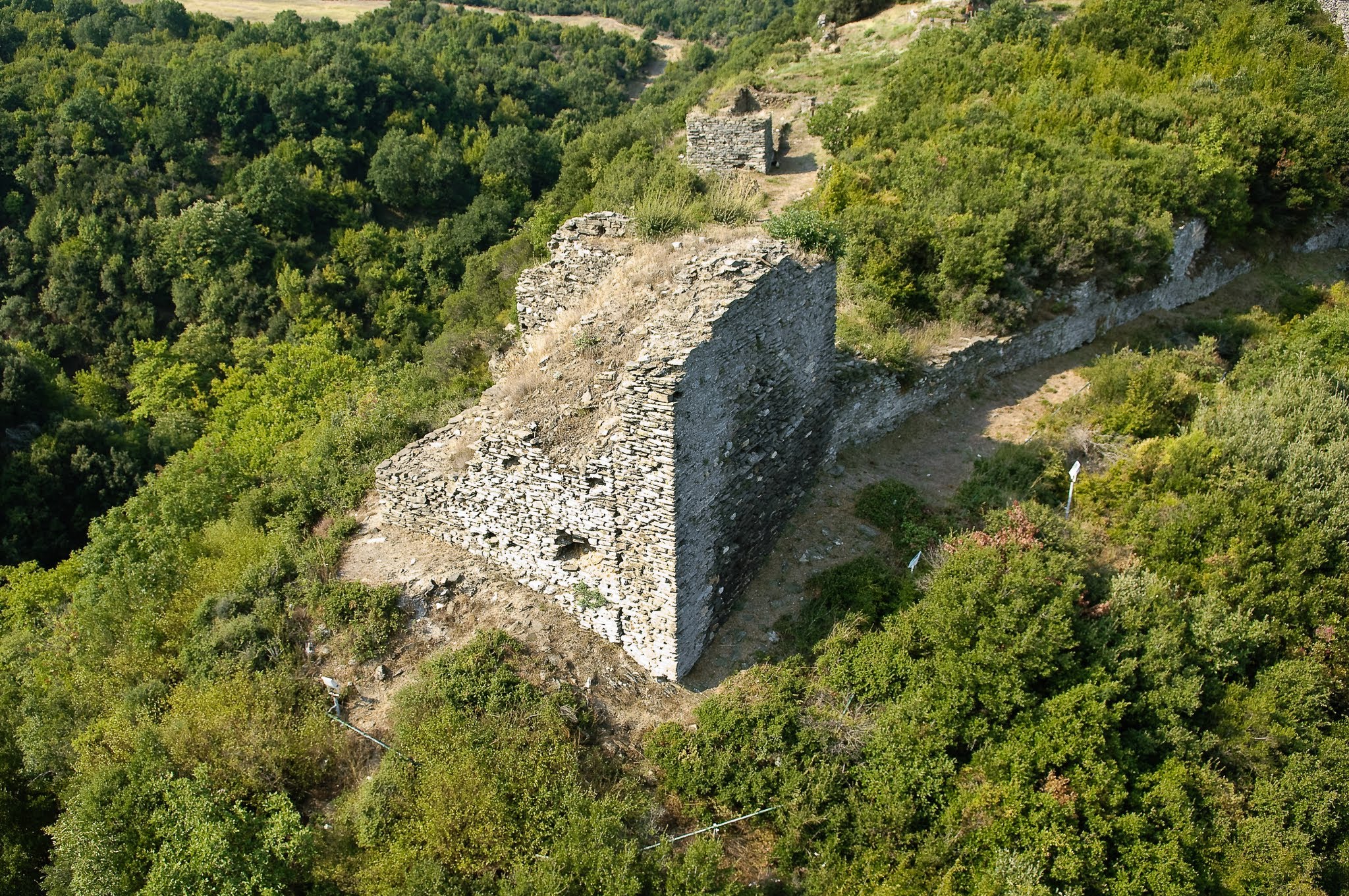 A high-angle close-up of a massive stone tower and defensive wall at the Castle of Rentina, detailing the ancient dry-stone construction.