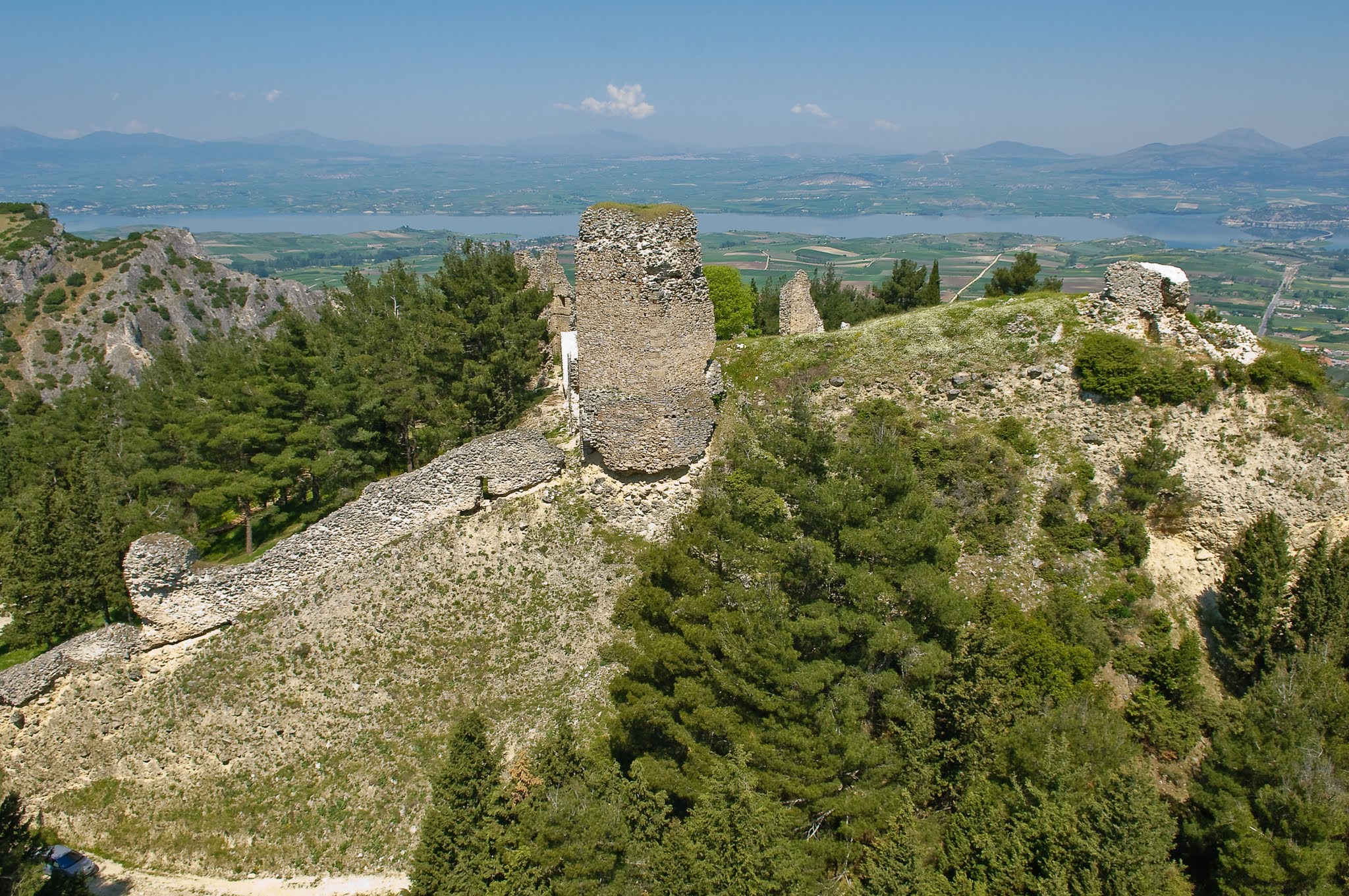 A wide oblique aerial photograph showing the central stone keep and defensive walls of the Byzantine Castle of Servia, overlooking the surrounding plain and Lake Polyfytos.