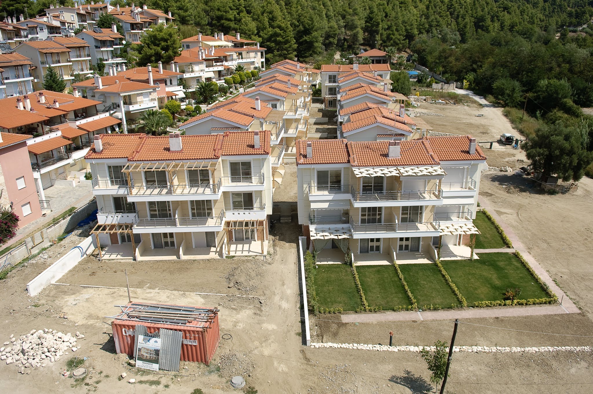 An aerial view of a new seaside residential development under construction, highlighting completed townhouses, landscaped lawns, and active building sites.